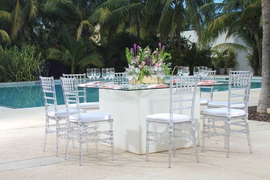 Mesa blanca junto a la alberca con sillas Tiffany transparentes