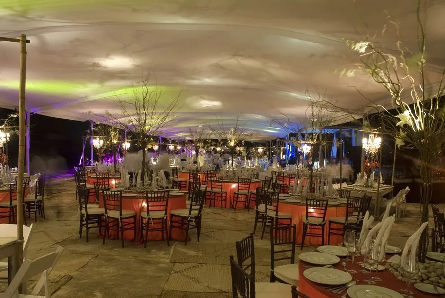 Carpa de noche con mesas redondas, mantelería naranja y sillas de madera